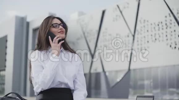 时髦的女人在智能手机上说话坐在她办公室附近的长凳上视频的预览图