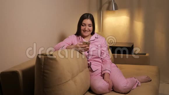 一个穿着睡衣的女人坐在沙发上手机放在灯的背景下视频的预览图