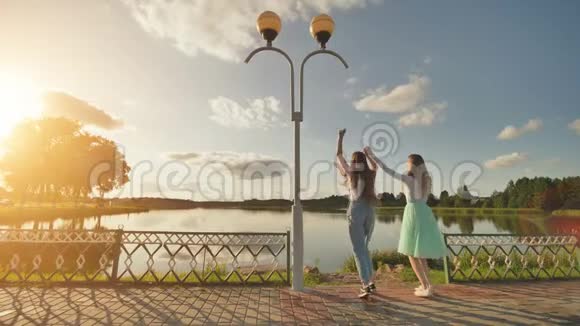 两个姐妹在夏日夕阳和湖面的背景下跳跃视频的预览图
