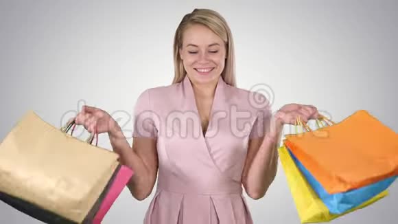 兴奋的漂亮年轻女士站着看相机在梯度背景上显示购物袋视频的预览图