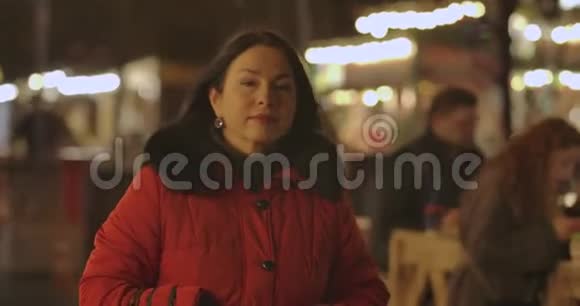 积极的白人妇女穿着红色外套在晚上沿着城市市场走来走去环顾四周成年女士肖像视频的预览图