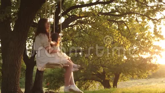 快乐的妈妈在日落时在橡树上的公园里的秋千上滚动一个有趣的婴儿幸福家庭的概念单身母亲视频的预览图
