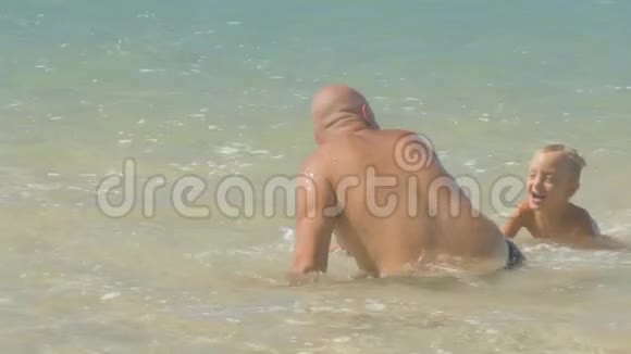 可爱的男孩抓住有趣的爸爸在平静的海水中玩耍视频的预览图