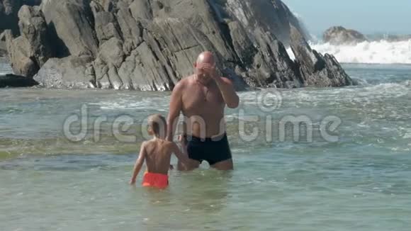 爸爸和小孩子在悬崖上享受清澈的海水视频的预览图