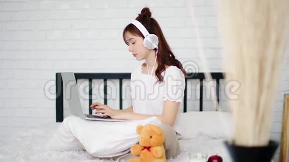 在床上打字时戴着耳机的漂亮女人视频的预览图