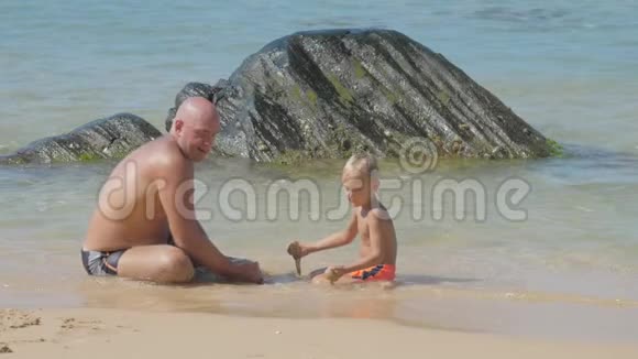 小儿子和爸爸在冲浪线上玩湿沙子视频的预览图