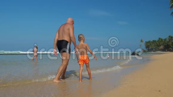 穿短裤的可爱男孩和爸爸沿着风景如画的海滩奔跑视频的预览图