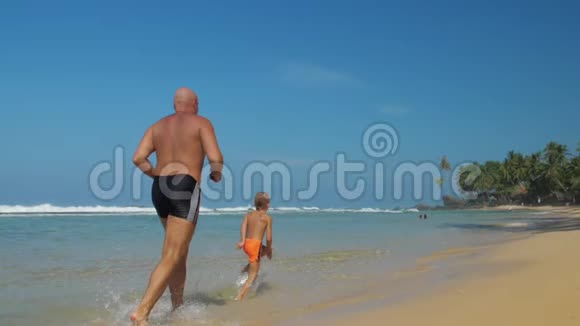 男孩和爸爸一家人在海滩的浅水中奔跑视频的预览图