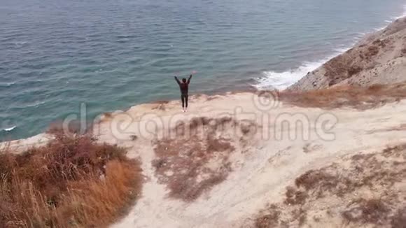 一个年轻的女人站在海边的悬崖边上练习瑜伽阿萨纳视频的预览图