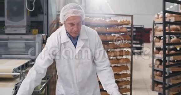 穿着白色制服的面包师把面团架装到面包店的其他部分大的视频的预览图