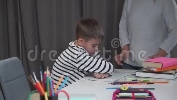 一个精疲力竭的白人男孩坐在桌子旁母亲责备他淘气的儿子拒绝学习或视频的预览图