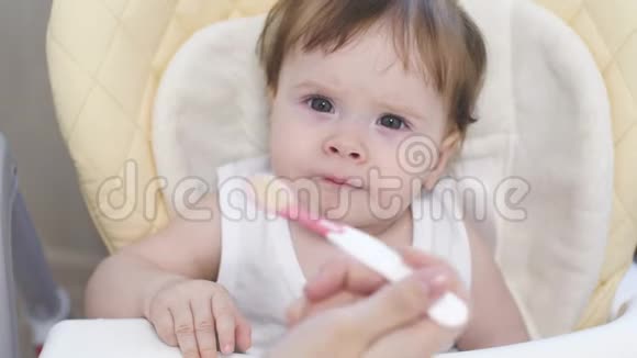 快乐宝宝用勺子吃第一顿饭妈妈用小勺子喂宝宝孩子坐在一个现代化的婴儿里视频的预览图