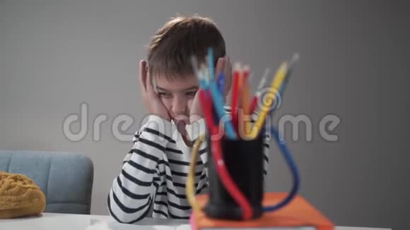 精疲力竭的白人困男孩坐在学校的桌子旁小学生用手抱着他的头厌倦无聊的孩子视频的预览图
