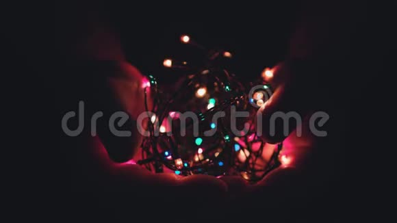 在黑暗的背景下用男性手中的灯光燃烧着节日的圣诞花环选择性聚焦模糊复古色调视频的预览图