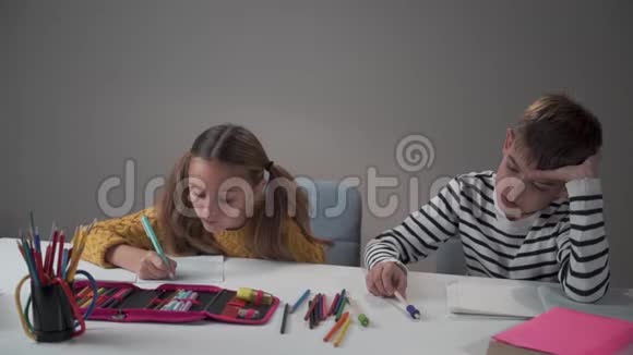 无聊的白人男孩坐在他勤奋的同学旁边在作业本上写下马尾辫的漂亮女孩视频的预览图