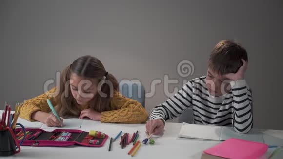 悲伤的白人男孩和快乐的女孩坐在学校或家里的桌子旁聪明的姐姐做家庭作业视频的预览图