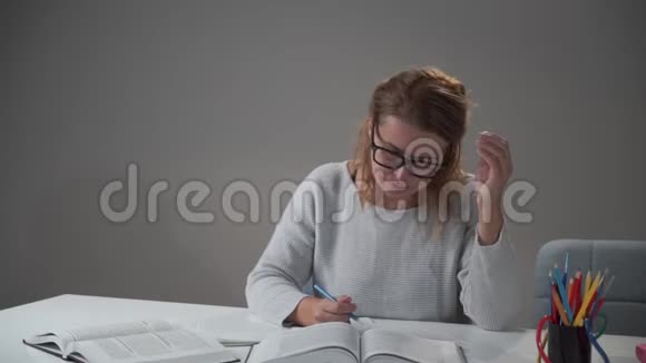 一位戴眼镜的白人年轻女子坐在桌子旁看书的肖像在家工作的漂亮成年女孩视频的预览图