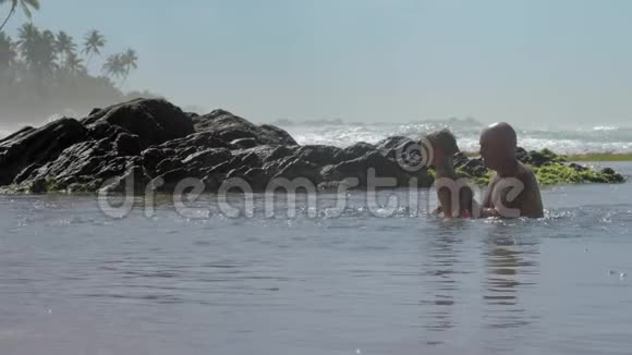 爸爸在异国度假胜地帮助儿子在平静的海水中跳跃视频的预览图
