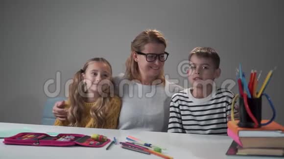 快乐的年轻白种人老师和她聪明的学生坐在桌子旁摆姿势戴眼镜的漂亮家教视频的预览图