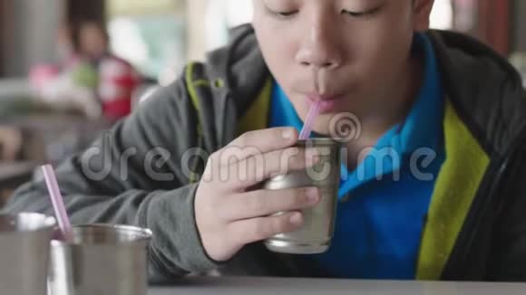 一个亚洲小男孩坐在家里用塑料管喝水视频的预览图