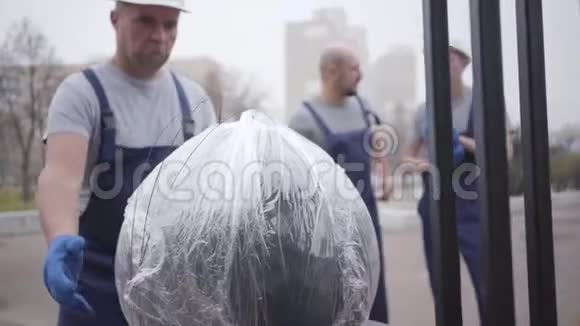 成年白种人戴着白色头盔和制服带着包裹步行到大楼上班的肌肉接生员视频的预览图