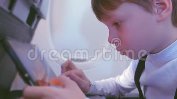 男孩在飞机上飞行时在平板上玩视频的预览图