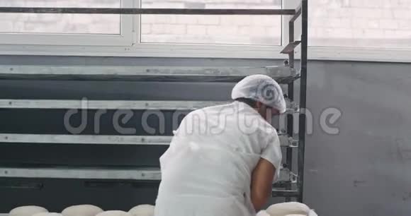 两名工人仔细地把面包从架子上装进了工业烤箱他们在一台机器里工作视频的预览图