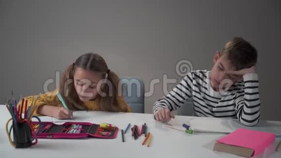 一个男孩在桌子上扔钢笔的肖像他那勤奋的妹妹惊讶地看着他继续写着视频的预览图