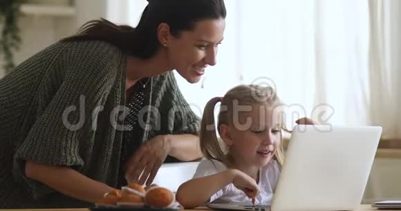 小女孩用笔记本电脑和妈妈控制厨房餐桌视频的预览图