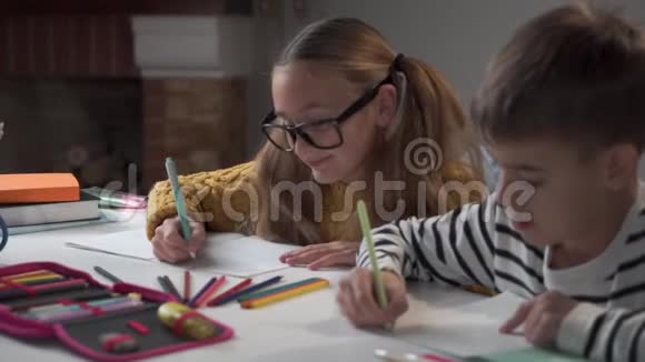 两个高加索同学坐在桌边写练习本戴眼镜的女孩看着男孩视频的预览图