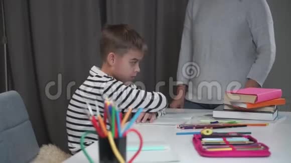 一个悲伤的白人小学生坐在桌子旁当他的老师责备他时淘气的男孩失败了视频的预览图