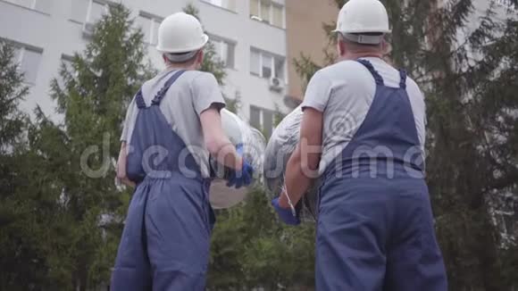 两名戴着白色头盔和蓝色制服的白人工人的背面视图男人互相看着视频的预览图