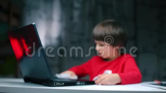 男孩坐在桌子旁用餐巾擦手提电脑视频的预览图