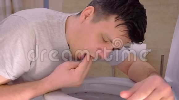 坐在地板上的厕所里的男人呕吐的肖像嘴里有两个手指视频的预览图