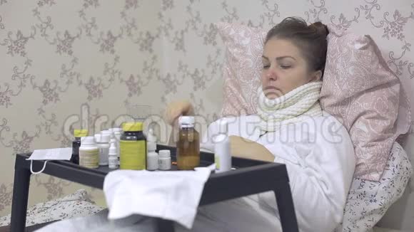 一位感冒的妇女躺在床上桌上摆着很多药喝着止咳药视频的预览图