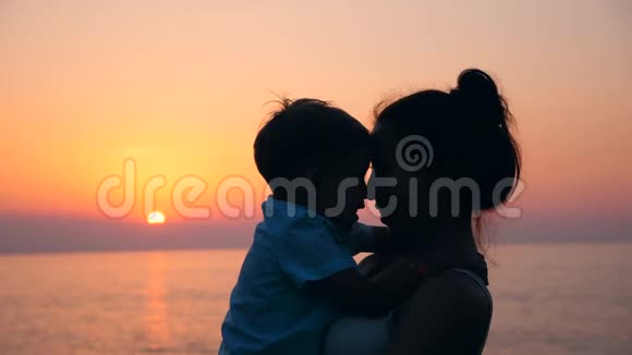 一个孩子和他的母亲在日落时拥抱和亲吻母亲和婴儿母性概念视频的预览图