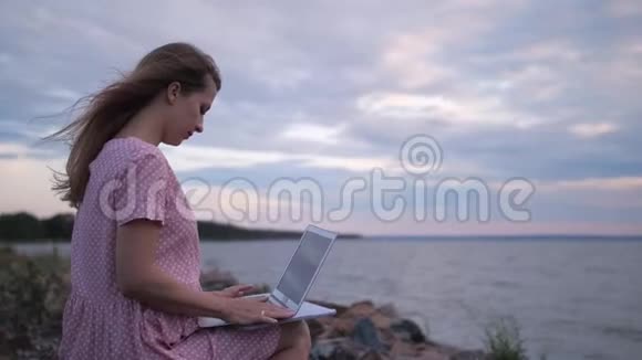 在海边的海滩上用笔记本电脑工作的女孩风把她的头发吹得很漂亮4K慢慢视频的预览图