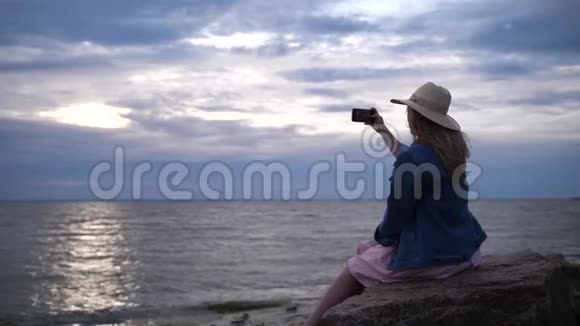 戴帽子的女孩给大海上的日落拍照4K慢慢视频的预览图