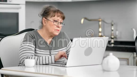 在家中厨房里用笔记本电脑进行有针对性的老年女性聊天视频的预览图