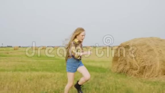 在秋村的干草堆上十几岁的女孩在收割田里奔跑穿牛仔裤的可爱女孩视频的预览图