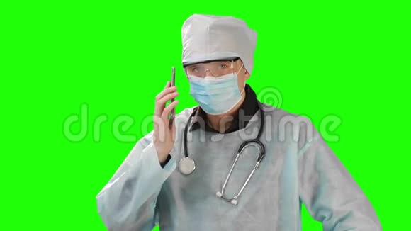 年轻医生戴着医用口罩和防护服打电话在Chrome按键背景下拍摄视频的预览图