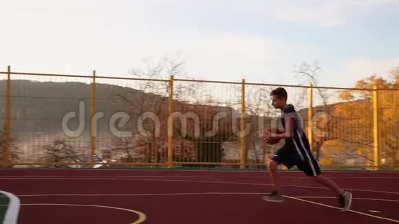 体育和篮球一个穿着蓝色运动服的青少年领着球然后把球扔进篮子天空和树林视频的预览图