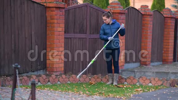 女孩用耙子从房子前面的草坪上摘下落叶视频的预览图