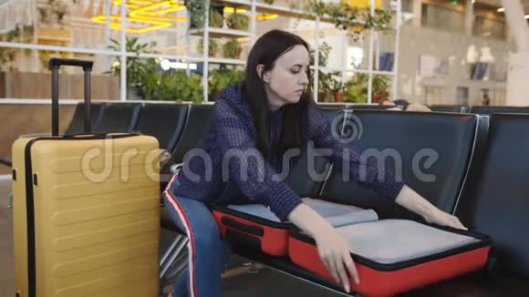 机场休息室里的女人在红色的大行李箱上拉链视频的预览图
