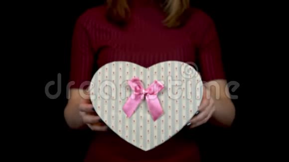 一个年轻的女人拿着一个心形的盒子对着相机女人手里拿着一件黑色背景的礼物视频的预览图