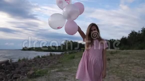 一个穿着粉红色裙子的年轻金发女郎带着球在海滩上散步然后她把球放到相机里4K视频的预览图