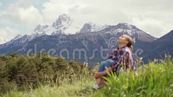 美丽的阿尔卑斯山景色和模糊的形象旅游妇女坐在绿色的草地上阿尔卑斯山的旅行视频的预览图