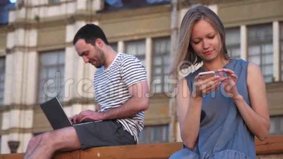 男人用笔记本电脑女人用智能手机坐在户外的长凳上视频的预览图