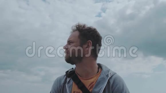 一个留着胡子的人站在靠近大海的云层背景上风会发展男人的头发4k4k录像60英尺视频的预览图