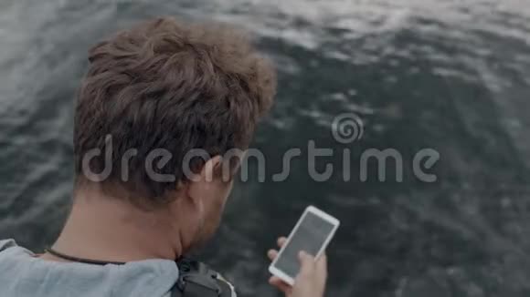 一个留着胡子的人坐在海中的一个码头上看着电话点击它从上面看4k4k录像60英尺视频的预览图